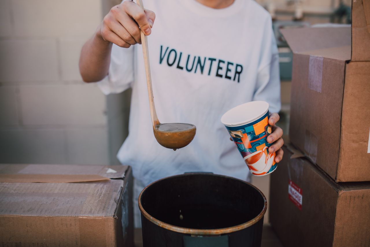 hero-img-01 A volunteer in a t-shirt serving soup at a community event. Helping hand.